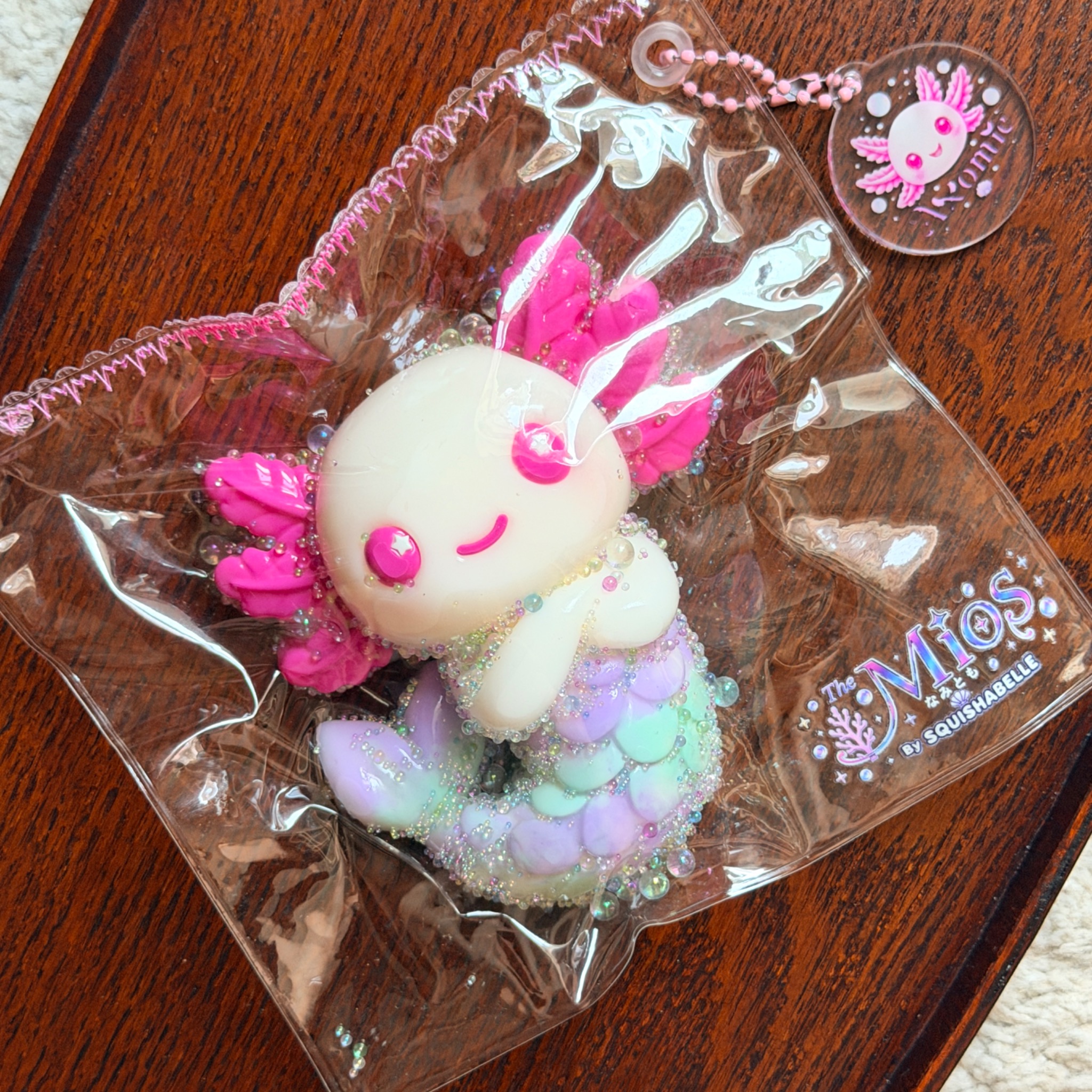 Axomie squishy in clear The Mios packaging on a wooden table